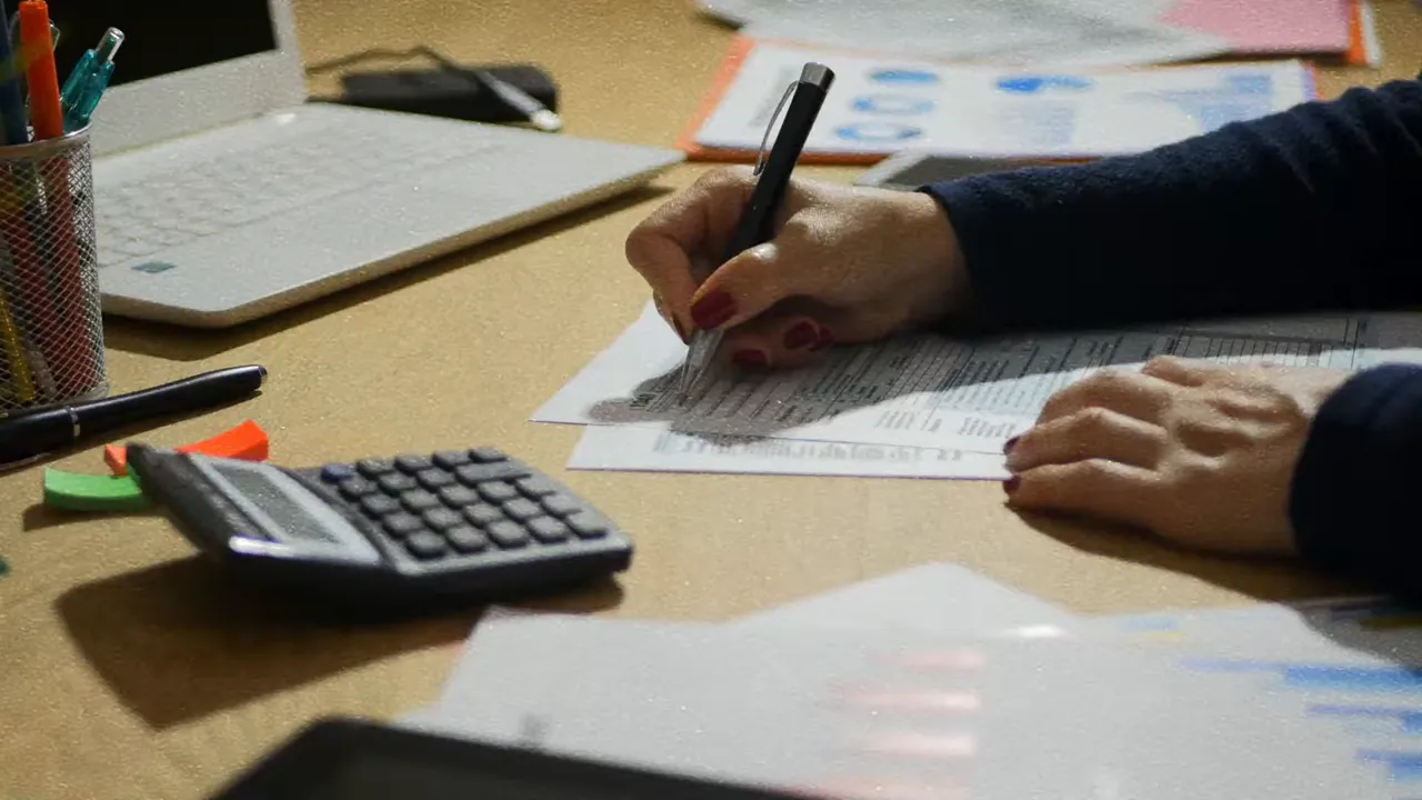 Hands filling out a tax form with a calculator on a desk