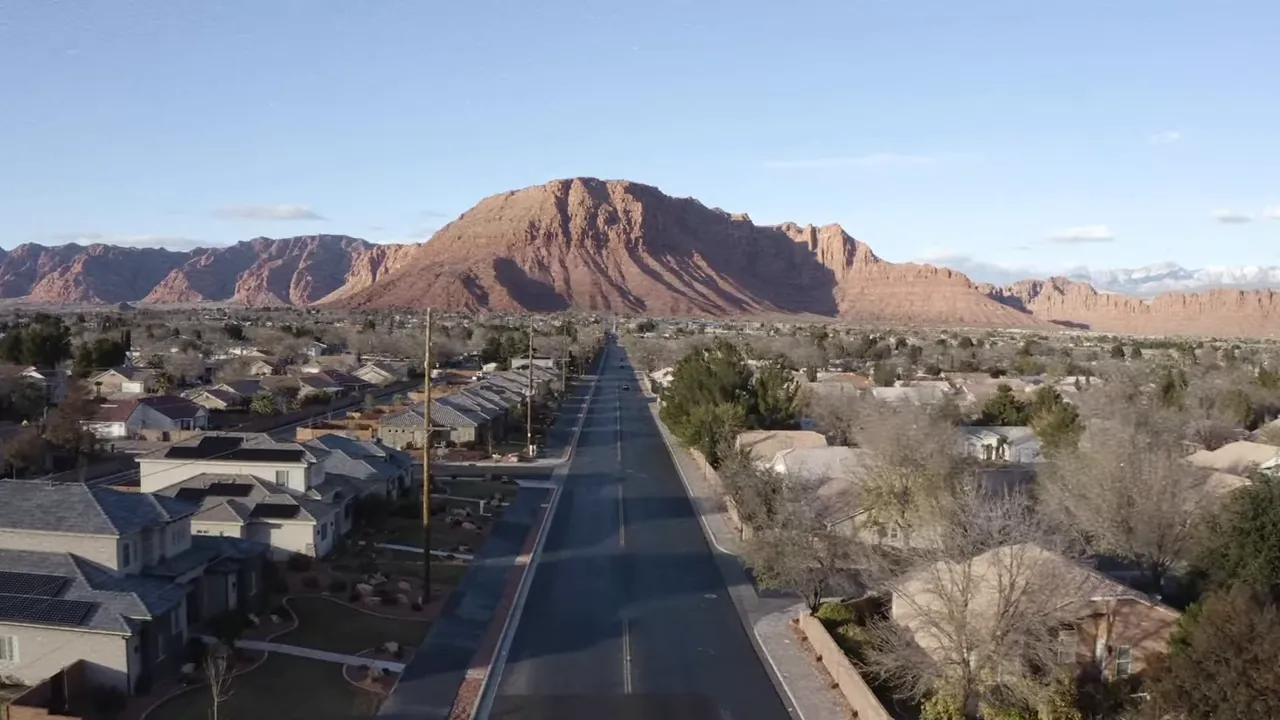 Clear aerial view of a suburban neighborhood and street with red rock mesas in the distance