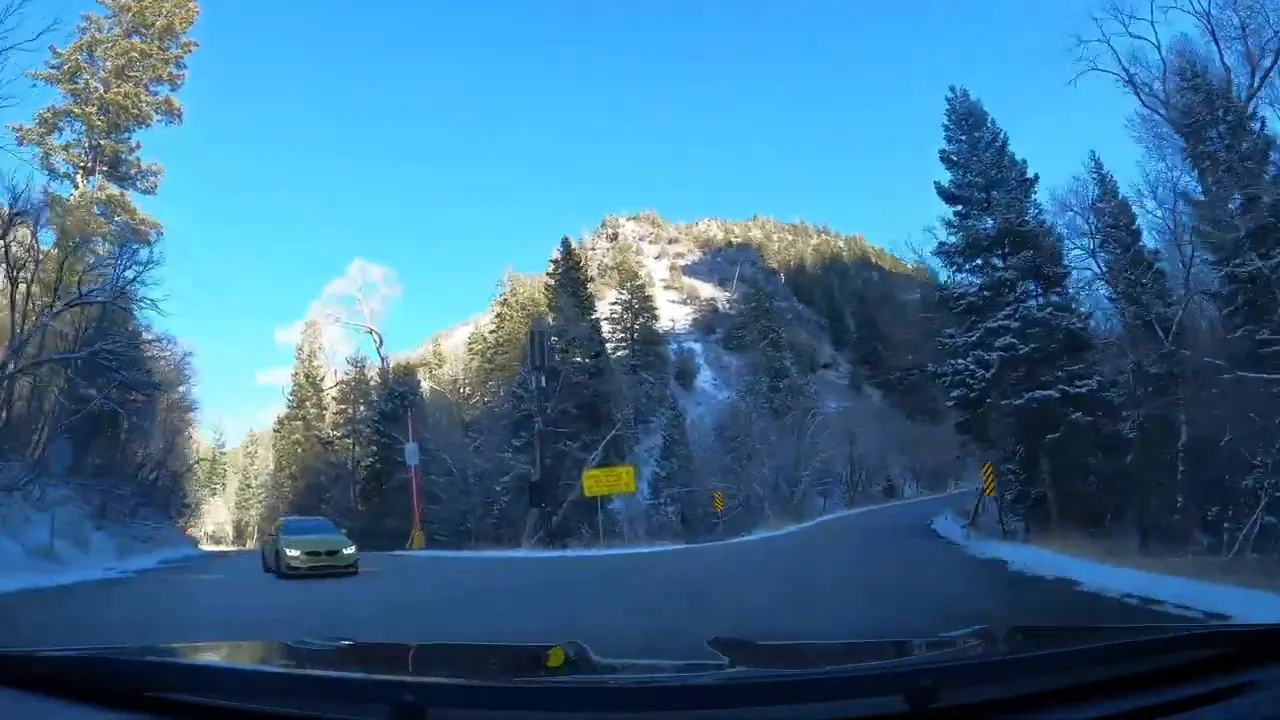 Winding mountain road into American Fork Canyon with snow on trees and a car approaching